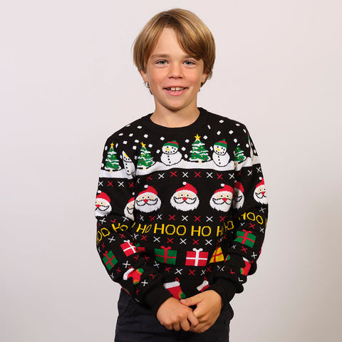 Et barn iført en sort julesweater med nissehoveder, snemænd og gaver på.