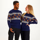 En mand og en dame kigger på hinanden og er begge iført en blå julesweater med rensdyr på.